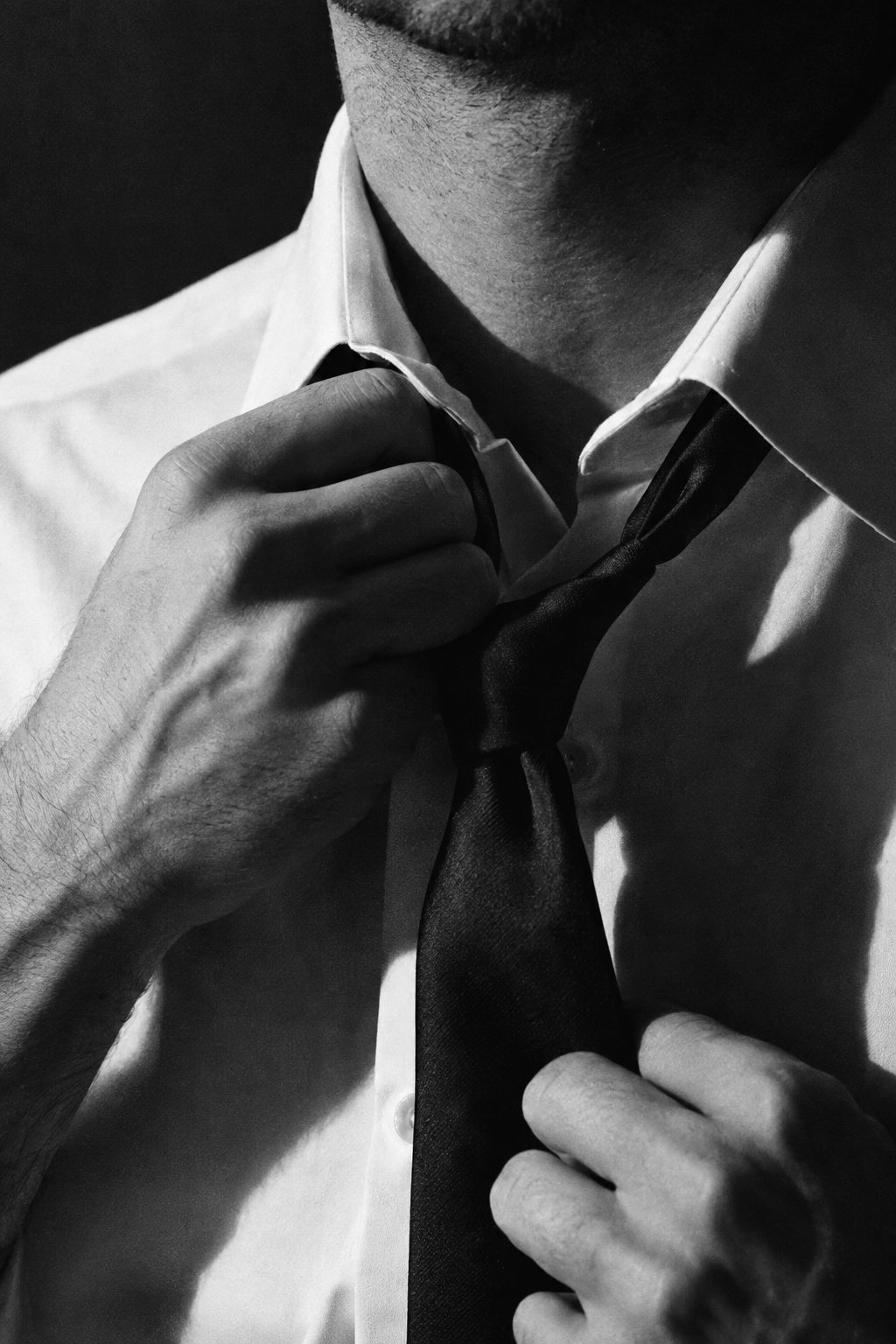 A man's hands loosening his tie in hard light